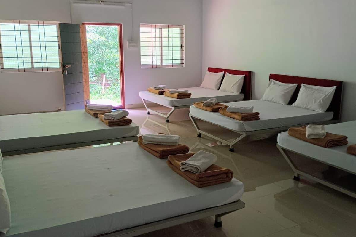 A hotel room with four single beds, each with a red headboard, and a small table with towels.