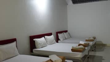 A hotel room with four beds arranged in a row, each with white linens and pillows.