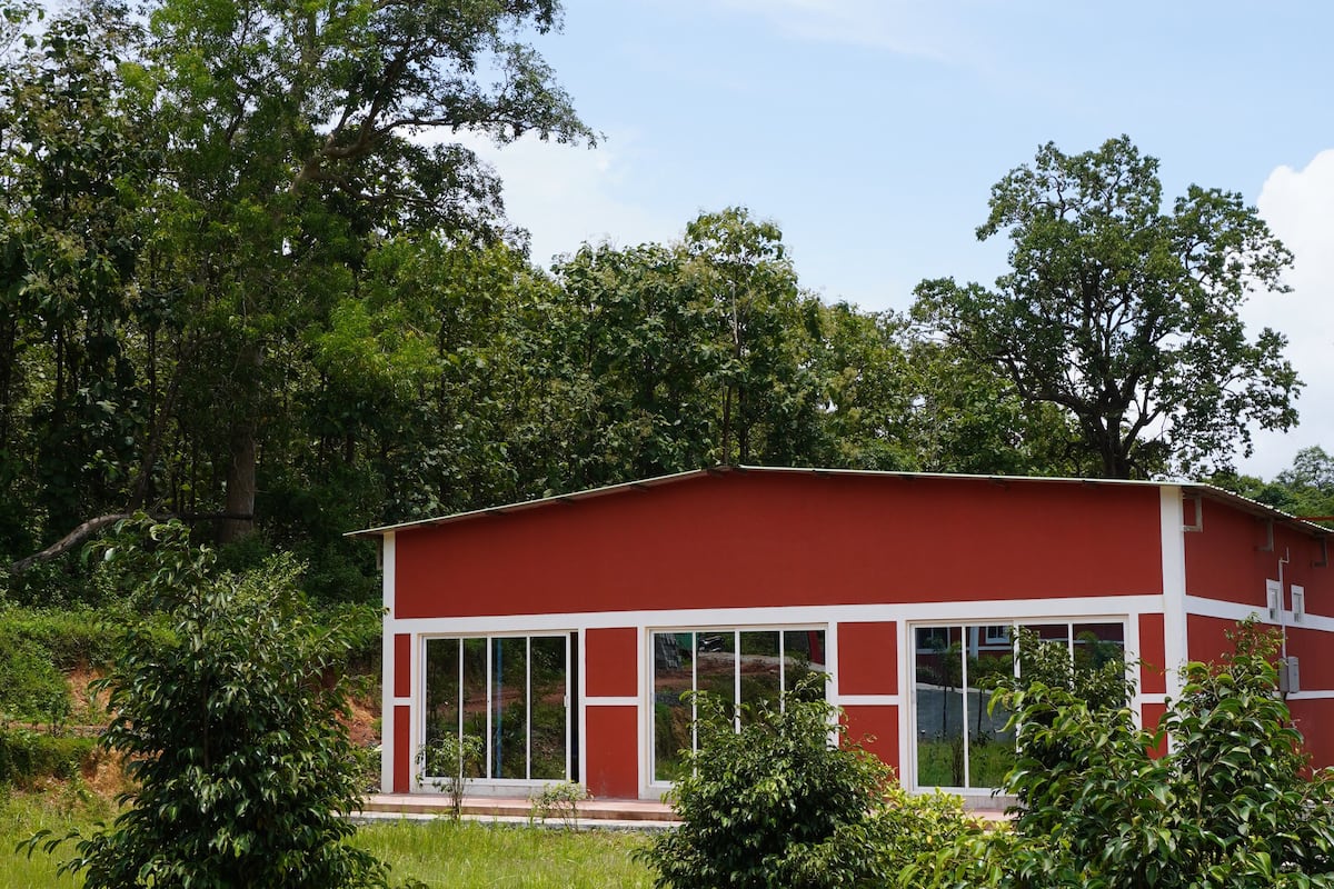 A red building with large windows, surrounded by greenery and trees.