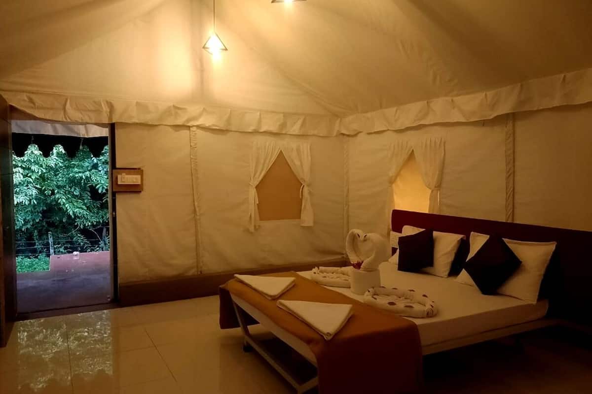 A tent-style room with a bed, pillows, a bedside table, and a window.