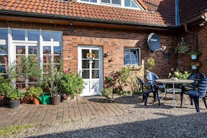 Et murstenshus med hvide døre, en parabolantenne og krukker med planter.