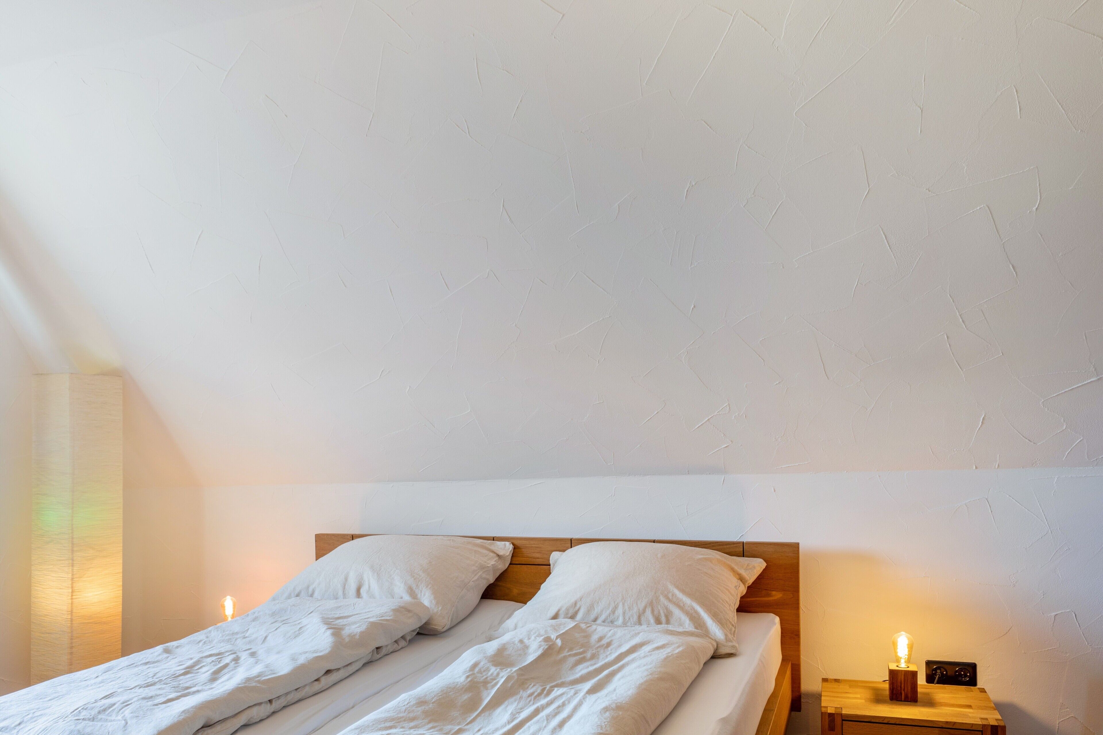 A double bed with white bedding, a wooden headboard, and a bedside table with a lamp.