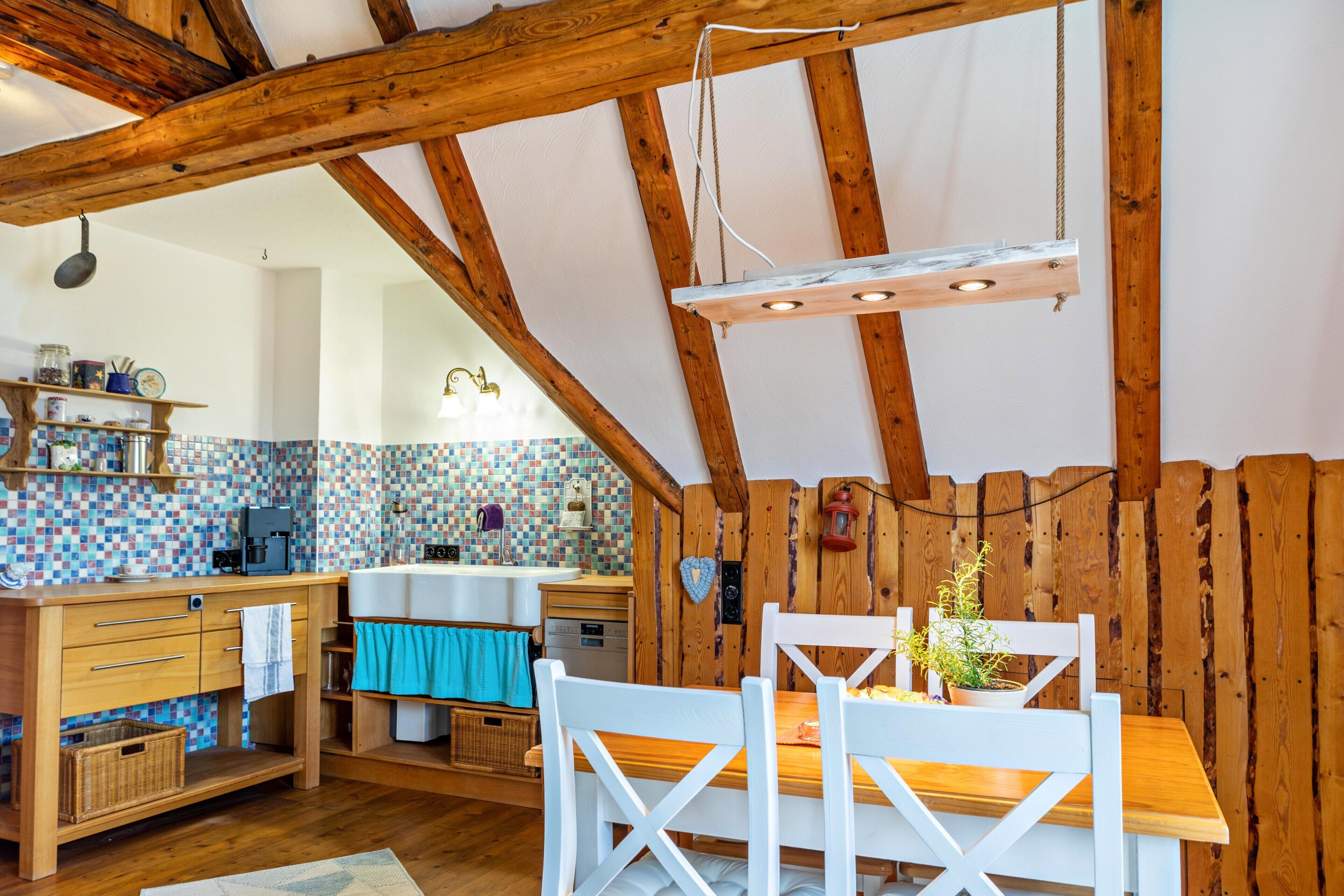 Una cocina rústica con vigas de madera, salpicadero de azulejos, una mesa de comedor de madera y sillas blancas.