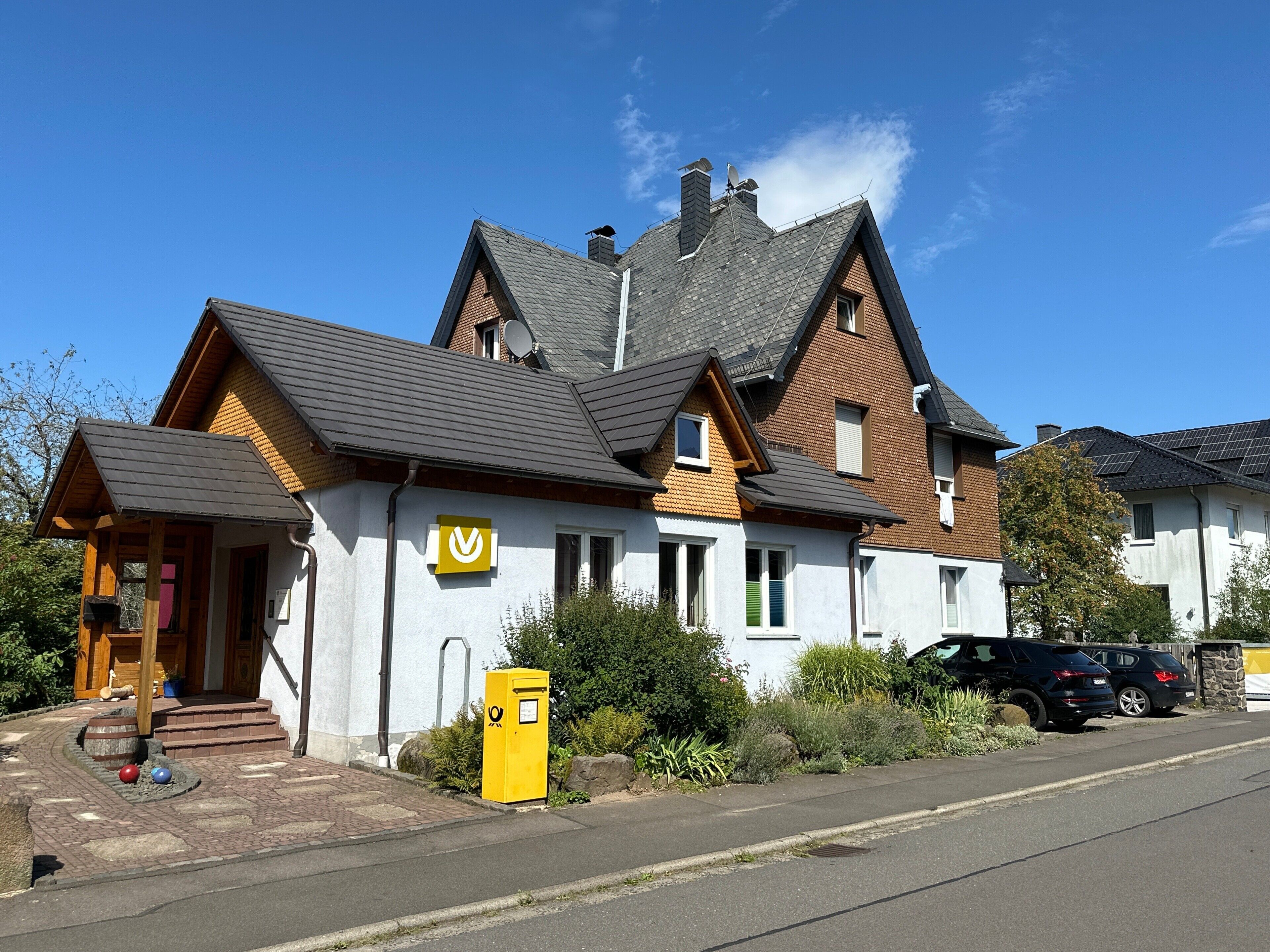 Een huis met twee verdiepingen, een schoorsteen, een schotelantenne en een brievenbus.