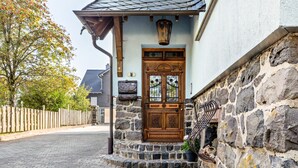 Ein Steinhaus mit Holztür, einer kleinen Veranda und einem Holzzaun.
