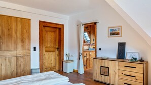 Ein Schlafzimmer mit Holzmöbeln, einem Bett, einer Kommode und Blick auf eine Küche und ein Badezimmer durch eine offene Tür.