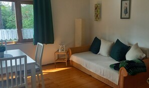 Une pièce comprenant un canapé, un fauteuil, une petite table, une fenêtre avec des rideaux et un tableau encadré accroché au mur.