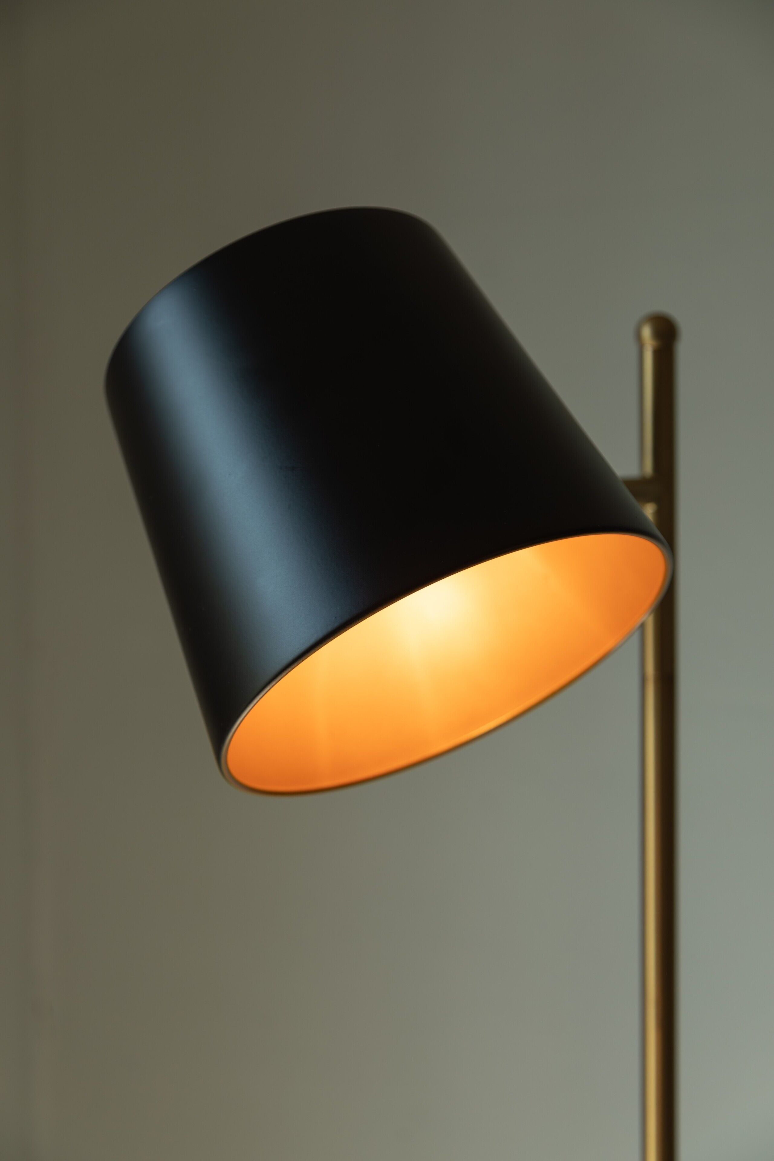 A lamp with a black shade and an orange interior, mounted on a gold stand.