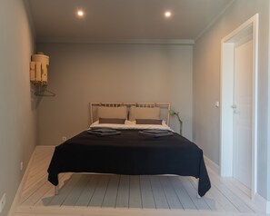 A bedroom with a bed, a bedside lamp, a wooden hanger, and a door. - Quiet Boutique Apartment with Courtyard Balcony (Großostheim)