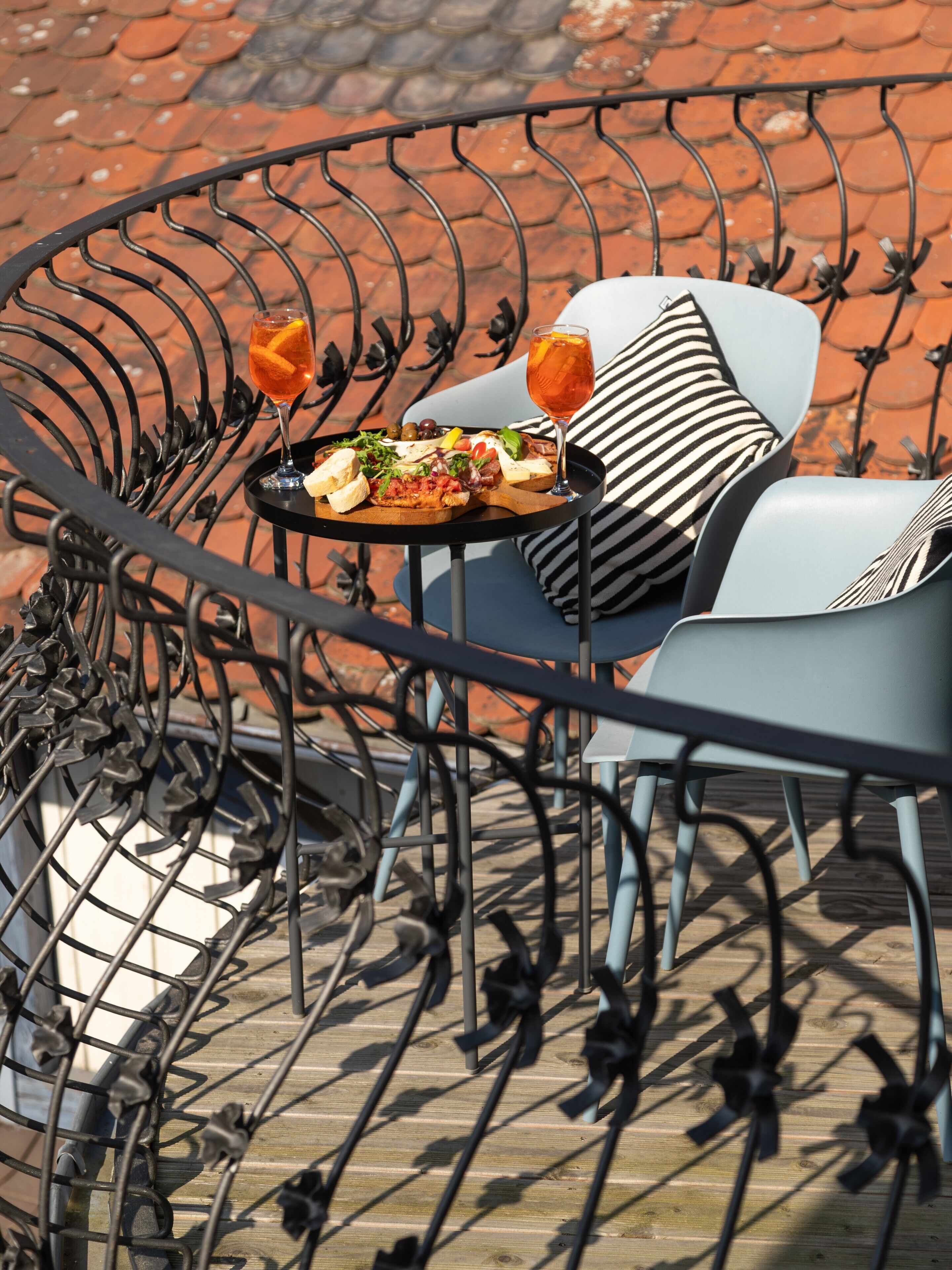 Een buitenzitgedeelte van metaal met een tafel gedekt voor een maaltijd, inclusief een bord eten en drinken.