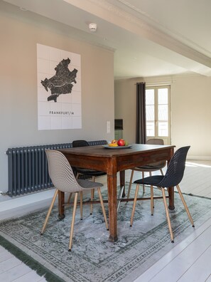 Un coin repas comprenant une table, des chaises, une assiette de fruits, une carte accrochée au mur et un radiateur.