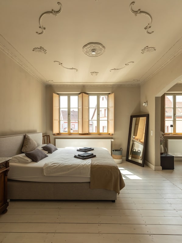 Une chambre à coucher avec un lit, une fenêtre, un radiateur, un miroir et un plancher en bois.