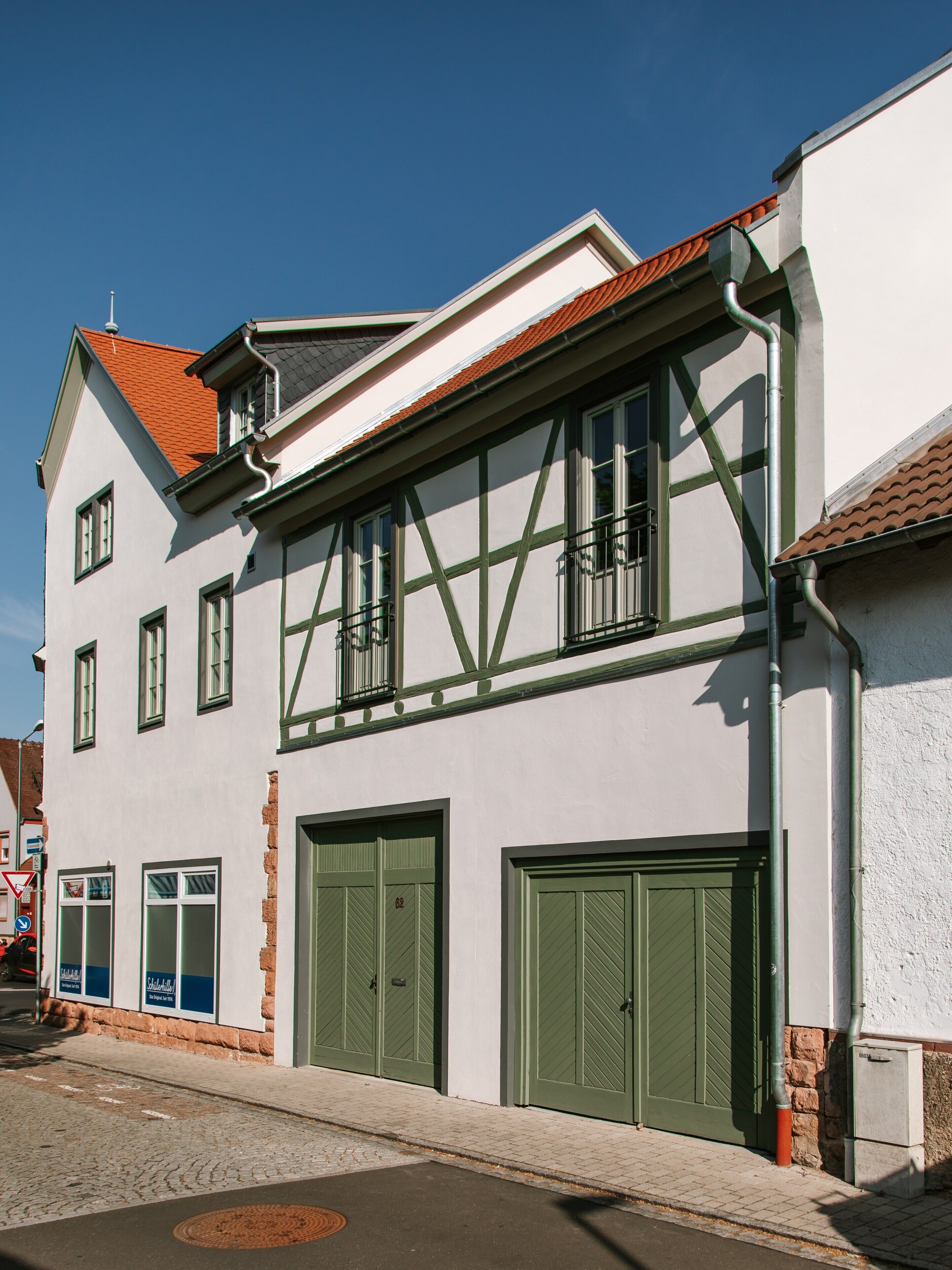A traditional building with a gabled roof, multiple windows, and a set of green double doors.