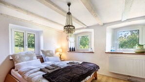A bedroom with a wooden bed, a chandelier, two windows with views of greenery, and a radiator. - Holiday Apartment Auf Dem Wald 6 Pers. with Mountain View, Private Terrace, and Wi-Fi (Görwihl)
