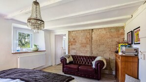 A bedroom with a large bed, a leather sofa, a chandelier, a brick wall, and a window with a view. - Holiday Apartment Auf Dem Wald 6 Pers. with Mountain View, Private Terrace, and Wi-Fi (Görwihl)