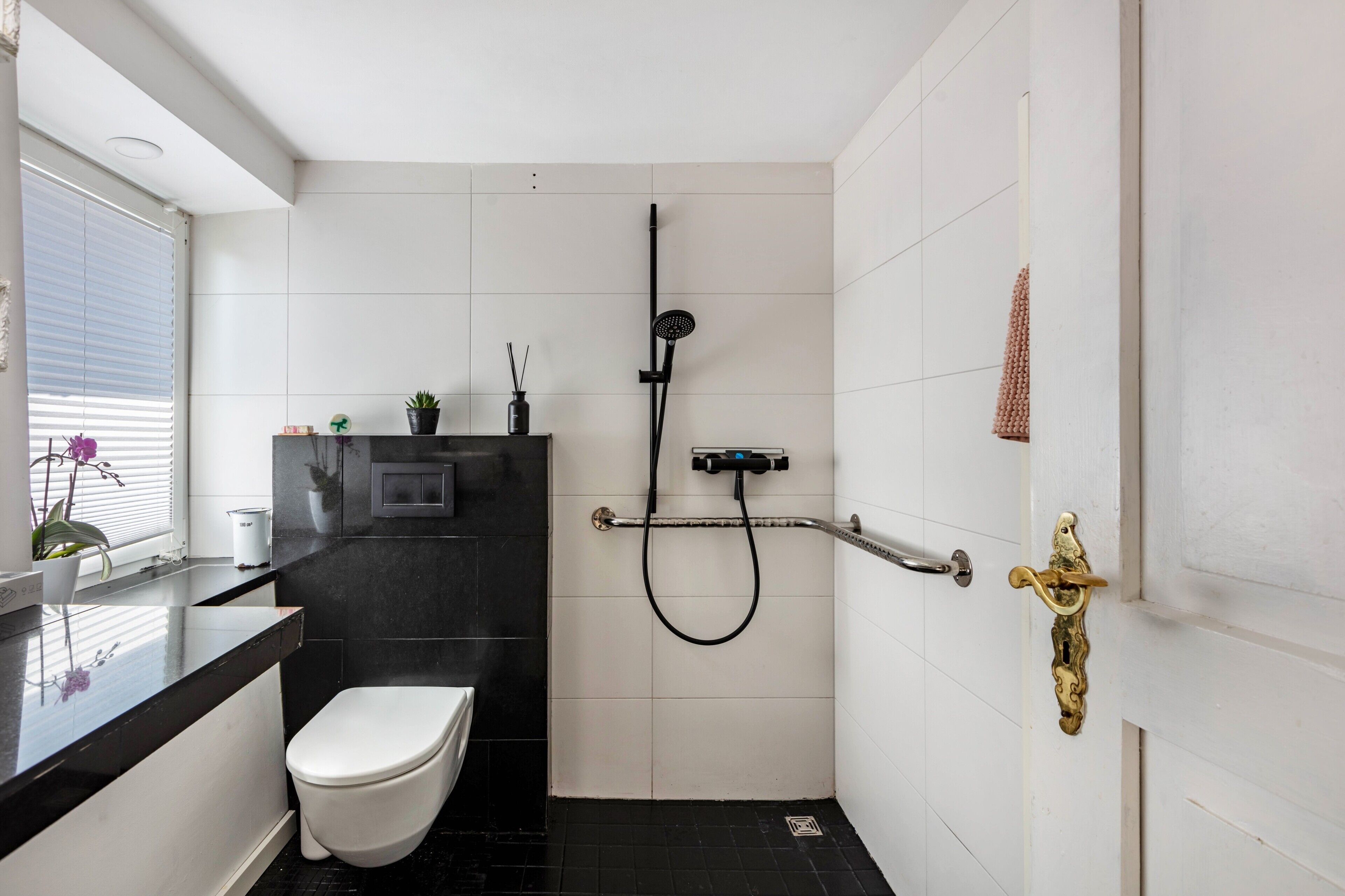 A bathroom with a toilet, a shower, a sink, and a window with blinds.