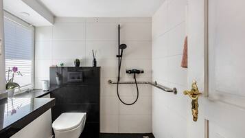 A bathroom with a toilet, a shower, a sink, and a window with blinds.