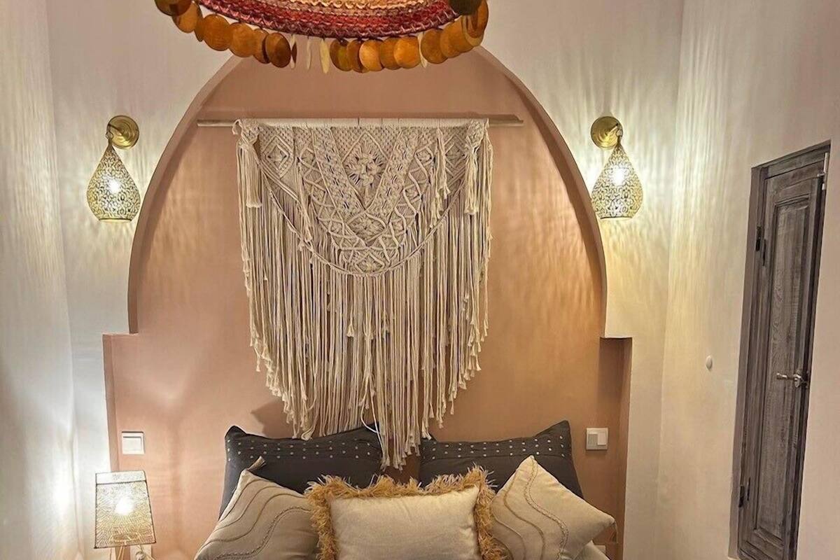 A bedroom with a bed, a macrame wall hanging, and a chandelier.