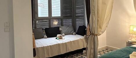 A room with a bed, a window with blinds, a hanging light fixture, and a patterned floor.