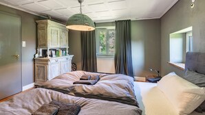 Een slaapkamer met een bed, een dressoir, een raam met gordijnen en een plafondventilator.