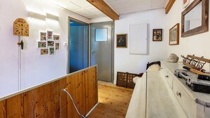 Een kamer met houten balken, een klok, lijstjes met foto's, een dressoir en een deur.
