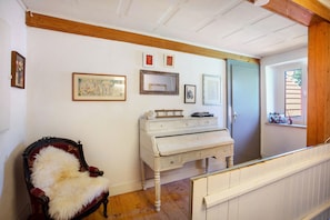 A room with a wooden ceiling, a white piano, a red armchair with a fur throw, and a door with a window.