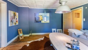 Een slaapkamer met een bed, een vachttapijt van koeienhuid, een bureau met waterflessen en kunstwerken aan de muren.