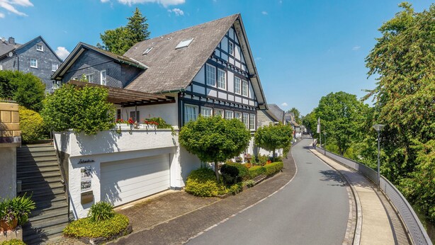 A traditional half-timbered house with a garage, a paved driveway, and a curved road with a sidewalk. - Apartment 'On the City Wall' with Private Terrace and Wi-Fi (Schmallenberg)