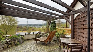 A covered patio with a wooden bench and table, stone flooring, and a view of the countryside. - Apartment 'On the City Wall' with Private Terrace and Wi-Fi (Schmallenberg)