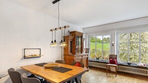 A dining area with a wooden table, chairs, a cabinet, and a view through large windows. - Apartment 'On the City Wall' with Private Terrace and Wi-Fi (Schmallenberg)