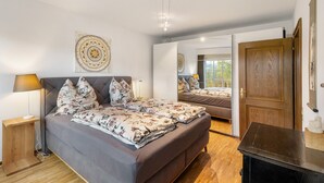 A bedroom with a bed, bedside table, lamp, and a mirror reflecting the room. - Apartment 'On the City Wall' with Private Terrace and Wi-Fi (Schmallenberg)
