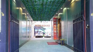 L’entrée d’un hôtel, avec une allée couverte, une enseigne rouge et deux voitures garées à l’extérieur.