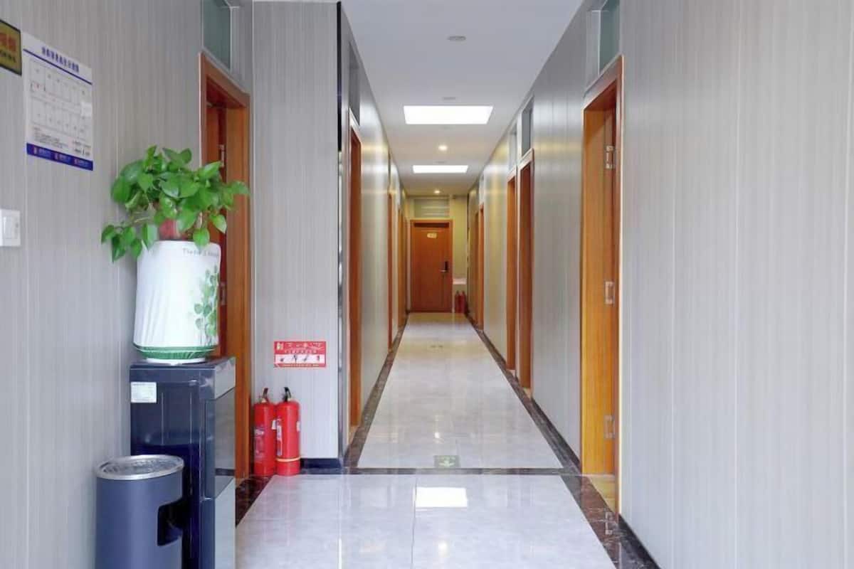 Un pasillo de hotel con un extintor, un cubo de basura y una planta en maceta.