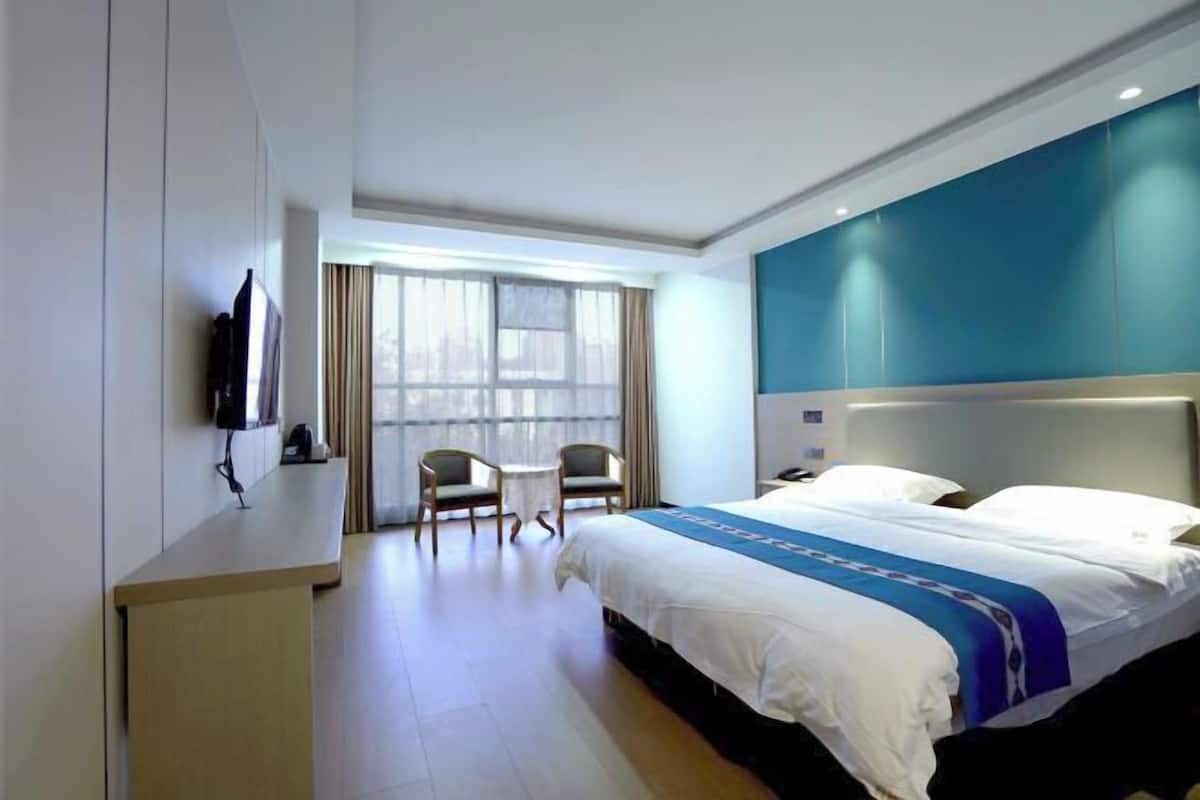 Habitación de hotel con una cama grande, un escritorio, una silla, un televisor y una ventana con cortinas.