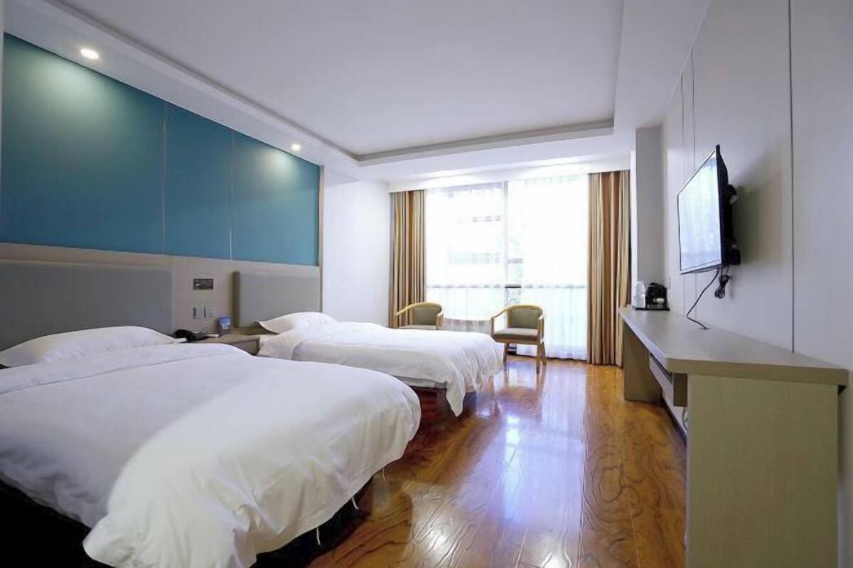 Habitación de hotel con dos camas, un escritorio, una silla, un televisor y una ventana con cortinas.