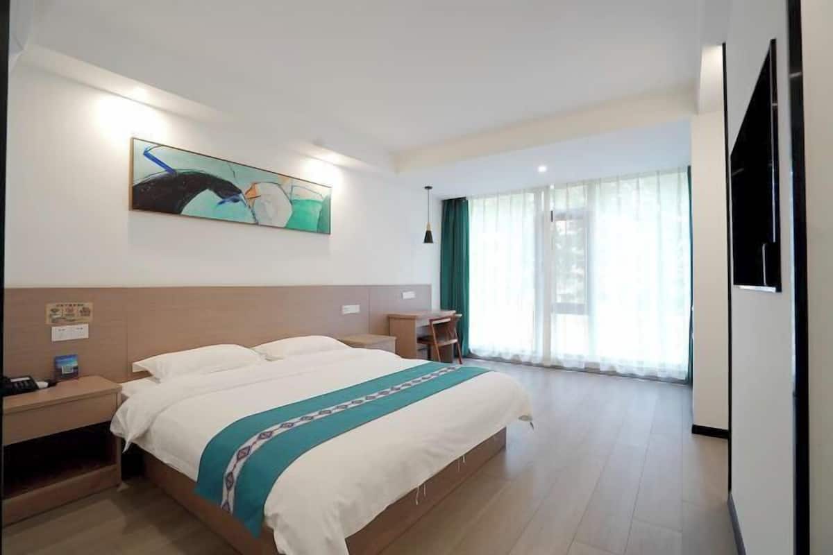 Habitación de hotel con una cama grande, un escritorio, una silla, un televisor y un cuadro en la pared.
