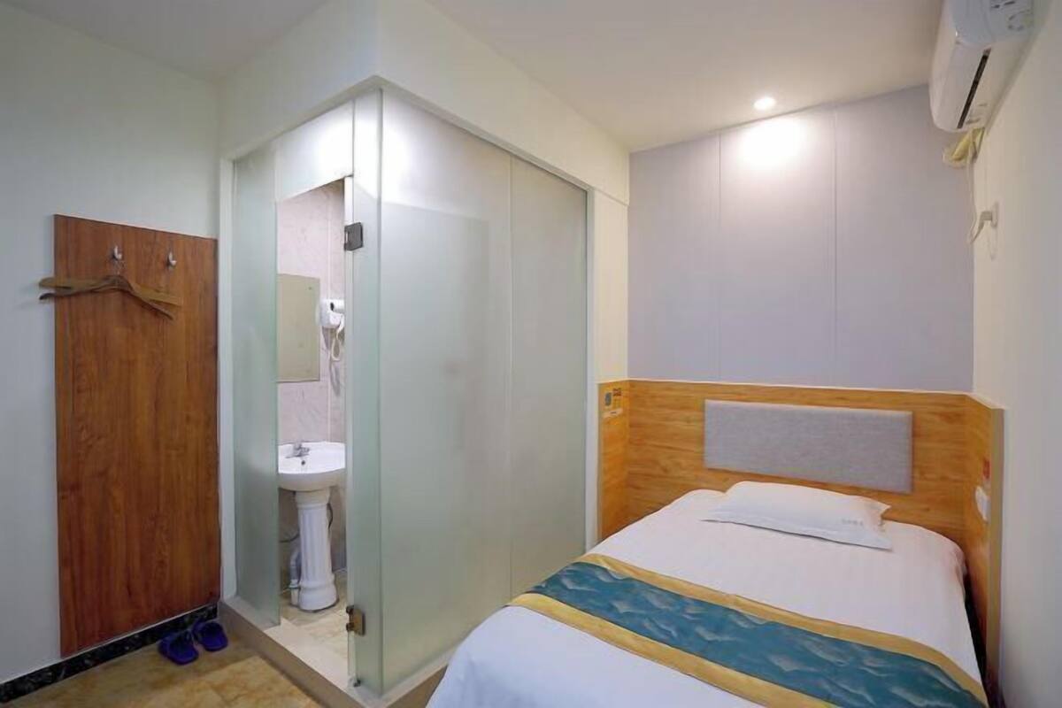 Habitación de hotel con cama, armario de madera, baño con lavamanos y ducha.