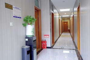 A hotel corridor with a vending machine, a potted plant, and fire extinguishers.