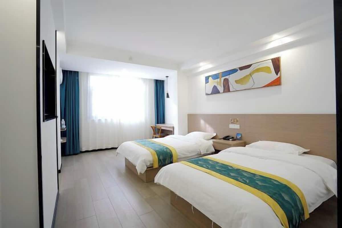 Habitación de hotel con dos camas, un escritorio, una silla, un televisor y un cuadro en la pared.