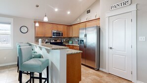 A modern kitchen with wooden cabinets, a stainless steel refrigerator, a microwave, and a bar area with stools.