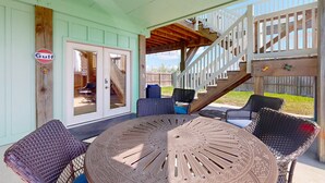 A covered patio with wicker furniture, a round table, and a staircase leading to an upper level.