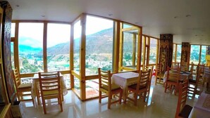A dining area with wooden chairs and tables, large windows offering a view of a mountainous landscape. - Hotel Oro Villa (Thimphu)