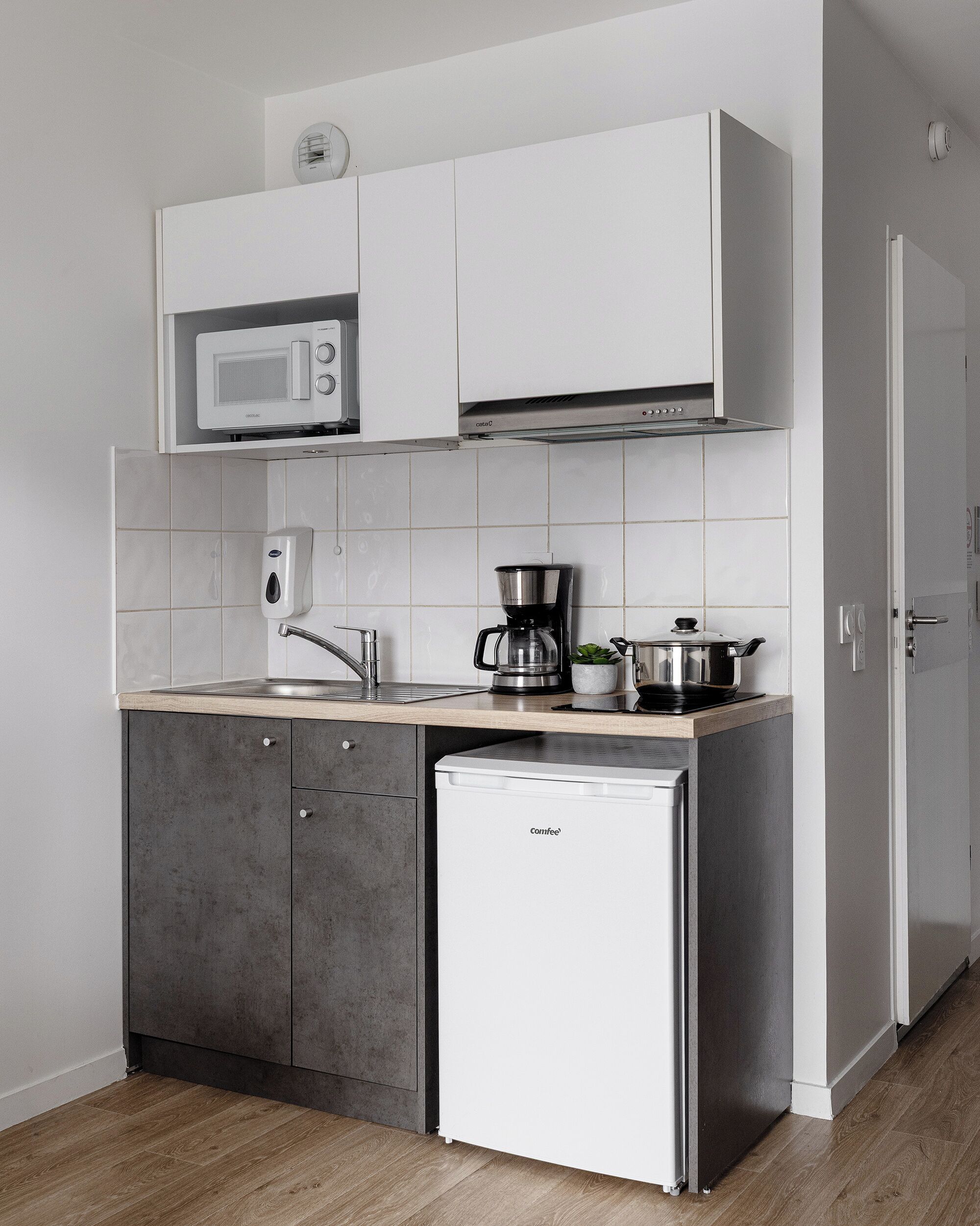 Une cuisine compacte avec des meubles blancs, un four à micro-ondes, une machine à café et un réfrigérateur.