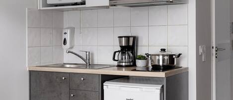 Une cuisine compacte avec des meubles blancs, un four à micro-ondes, une machine à café et un réfrigérateur.