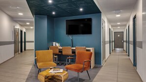 A modern hotel lobby with a blue accent wall, a flat-screen TV, and a seating area with orange chairs and a wooden coffee table. - Montempo appart-hotel Noisy le Sec  (Noisy-le-Sec)