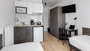 A compact hotel room with a kitchenette, a bed, a desk with a laptop, and a TV mounted on the wall. - Montempo appart-hotel Noisy le Sec (Noisy-le-Sec)