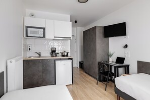 Habitación de hotel pequeña con kitchenette, una cama, un escritorio con una computadora portátil y un televisor montado en la pared.