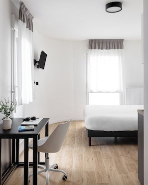 A modern hotel room with a bed, desk, chair, and a TV mounted on the wall.