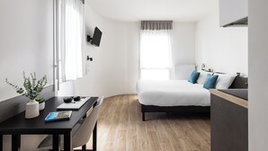 A modern hotel room with a bed, a desk with a laptop, a potted plant, and a window with curtains. - Montempo appart-hotel Noisy le Sec  (Noisy-le-Sec)