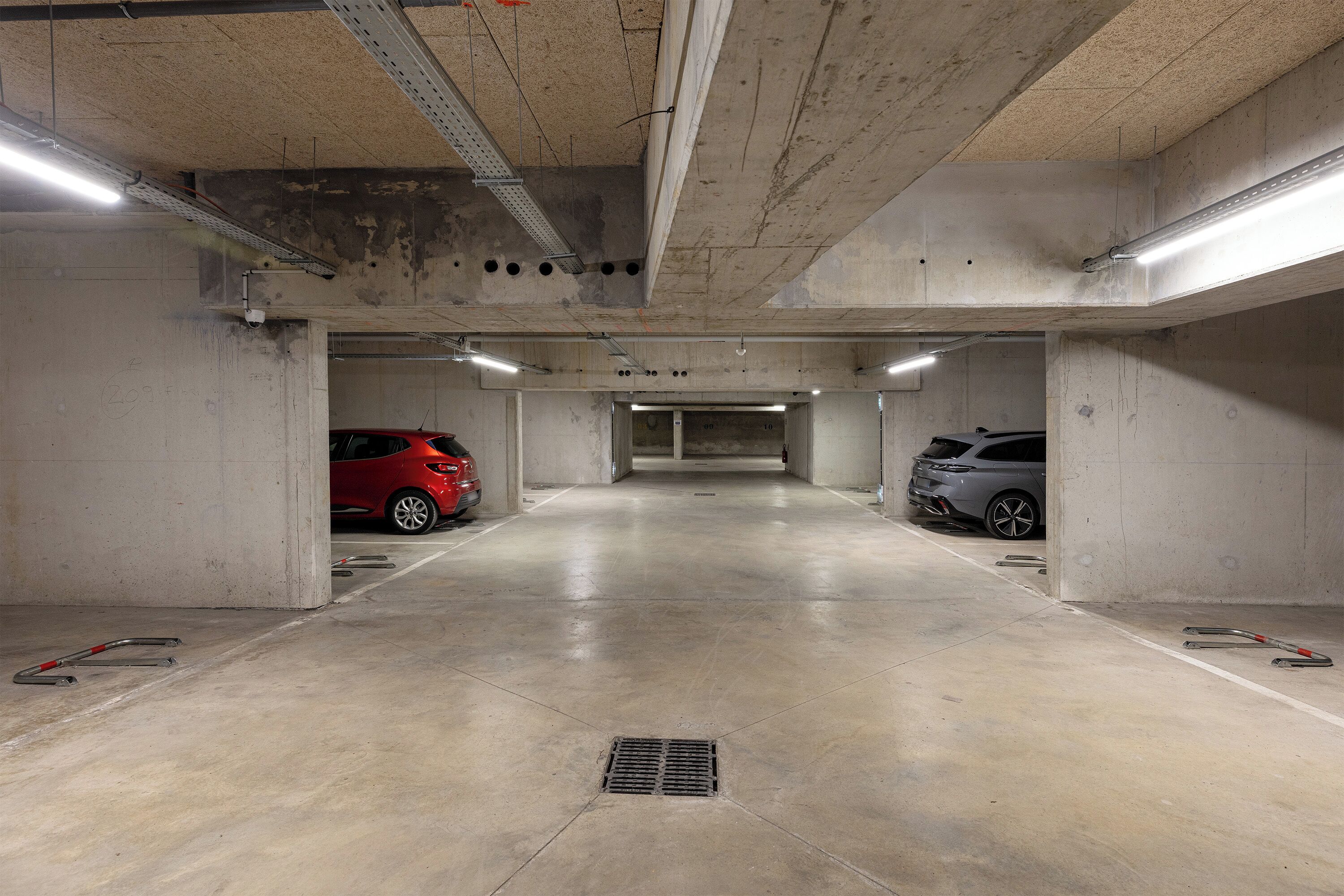 Un parking souterrain avec des murs en béton, un sol plat et un éclairage fluorescent au plafond.